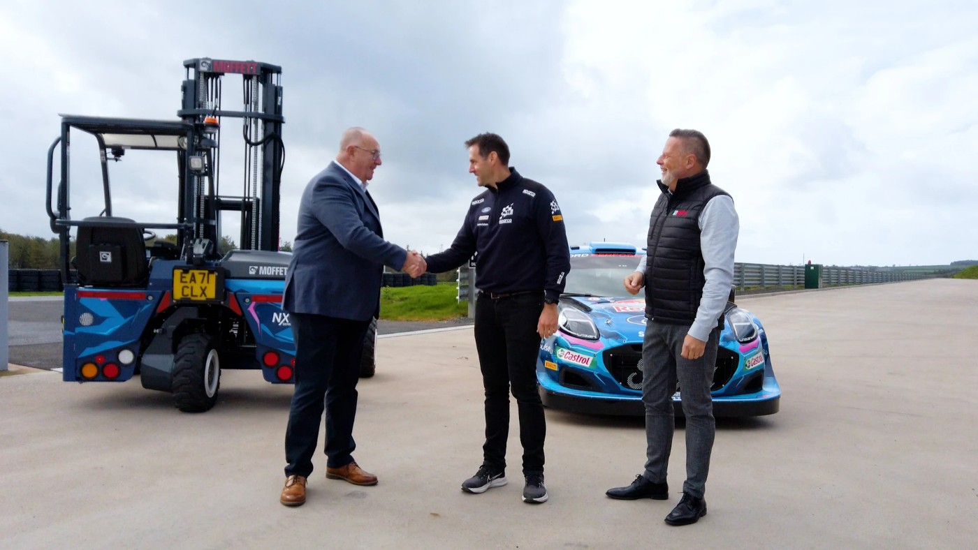 Two men shaking hands in front of a moffett forklift